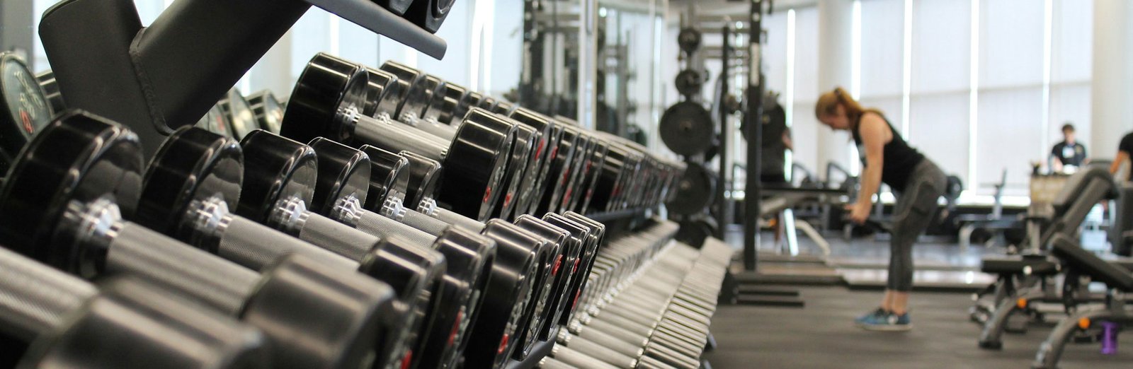 Gym Weights Rack Rack of dumbbells in a professional gym with a person training in the background